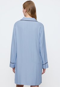 Completo pigiama in satin azzurro chiaro con texture a coste, maniche lunghe e bordi neri sul colletto e sui polsini, caratterizzato da una vestibilità comoda.