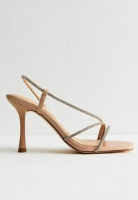 Nude högklackade sandaler med ett banddesign, prydda med rhinestones och fyrkantig tå. Materialet är slätt med en blank yta.