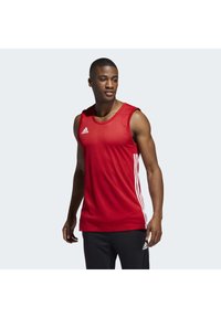 Débardeur de sport sans manches rouge avec une finition texturée, comportant des rayures blanches sur les côtés et un logo Adidas sur la poitrine gauche.