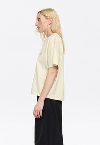 T-shirt di cotone giallo chiaro con maniche corte, vestibilità ampia, scollo rotondo e un sottile design ricamato sulla parte anteriore.