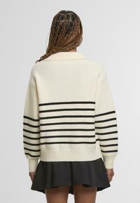 Krémový sveter s čiernymi horizontálnymi pruhmi, rebrovanými manžetami a golierom, doplnený čiernou rozšírenou sukňou.