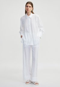 Witte overhemd met lange mouwen en kraag, met verticale strepen, gecombineerd met bijpassende wijde broek, beide met kleine metallic accenten.