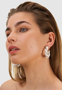 Weiße Keramikohrringe mit einem gedrehten Design, versehen mit goldenen Akzenten. Die glatte Textur und die abgerundete Form steigern die optische Anziehungskraft.