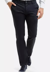 Czarne spodnie wykonane z gładkiego materiału, z prostą nogawką, zapięciem na guzik i bocznymi kieszeniami. Noszone z ciemnymi trampkami.