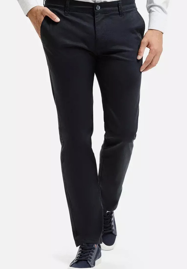 Czarne spodnie wykonane z gładkiego materiału, z prostą nogawką, zapięciem na guzik i bocznymi kieszeniami. Noszone z ciemnymi trampkami.