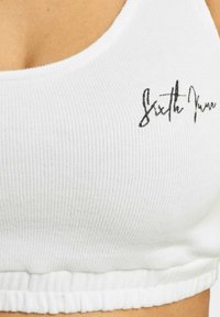 White ribbed crop top featuring a ruffled hemline and black embroidered text that reads "Sixth June." Soft texture and fitted design.