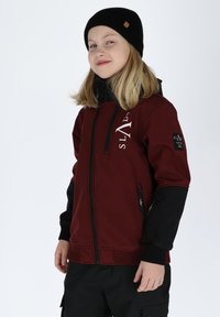 Red and black jacket with a zip closure, ribbed cuffs, and logo on the chest. Smooth texture, features side pockets and fabric patches.