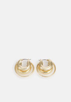 Paire de boucles d’oreilles créoles dorées avec un design circulaire en couches et une finition polie sur fond blanc.