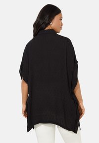 Svart, lättvikts oversized skjorta med texturerat mönster, korta ärmar och rundad nederkant. Har krage och avslappnad passform.