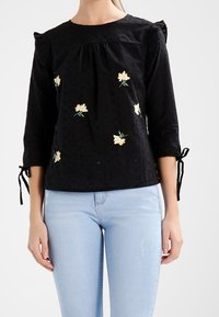 Černá bavlněná blůza se třičtvrtinovými rukávy, zdobená květinovou výšivkou v žluté a zelené. Obsahuje volánkové ramena a mačkané detaily.