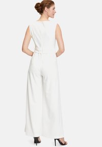 Melek sleeveless jumpsuit dengan bodice yang ketat, celana lebar, dan ritsleting belakang. Dipasangkan dengan sandal hak tinggi berwarna hitam.