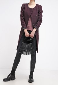 Dlouhý vínový kabát se strukturovaným designem, spárovaný s pleteným růžovým topem, tmavými džíny a černou kabelkou s tř�ásněmi. Černé šněrovací boty dotvářejí vzhled.