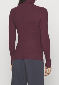 Burgunderröd ribbad polotröja med långa ärmar, med en figurnära silhuett och texturerat mönster, tillsammans med marinblå byxor.