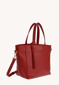 Sac à main en cuir rouge avec double poignée supérieure, une sangle d'épaule amovible et un pendentif décoratif sur une surface lisse et texturée.