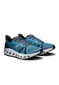 Baskets de sport bleues en mesh et matériaux synthétiques, avec une semelle blanche rembourrée aux accents noirs et un système de laçage.