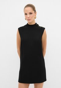 Vestido negro sin mangas con cuello alto, textura suave y acentos de botones dorados en el hombro. Diseño de corte recto.