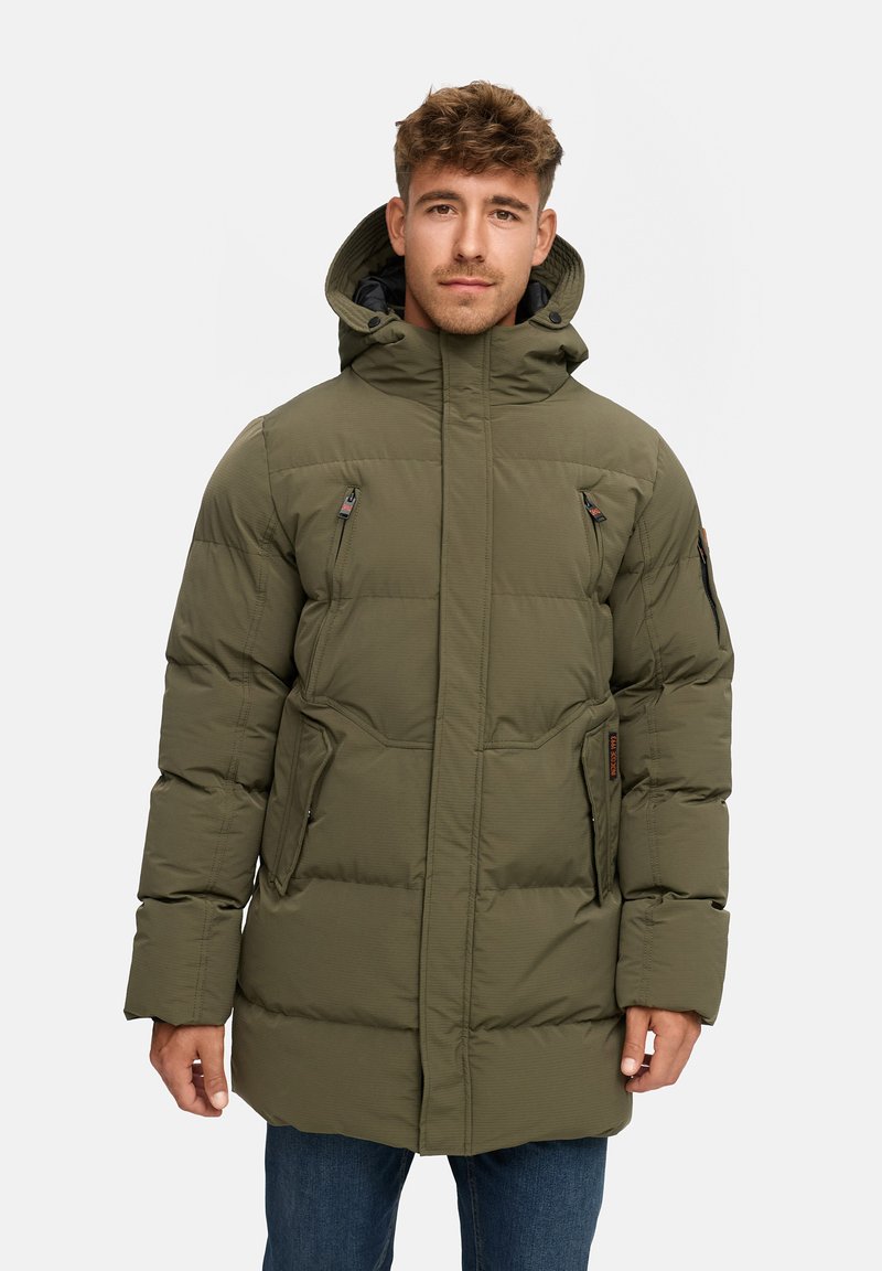 Parka acolchado verde con capucha, con bolsillos con cremallera y un acabado texturizado, llevada sobre unos vaqueros.