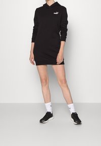 Vestido con capucha negro hecho de tejido suave, con mangas largas, un bolsillo canguro y un pequeño logo blanco en el pecho.