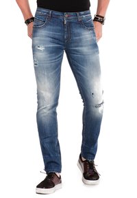 Lichtblauwe denim jeans met een slim fit, versleten details en vervaagde stukken. Heeft vijf zakken en een rits, gecombineerd met donkere sneakers.