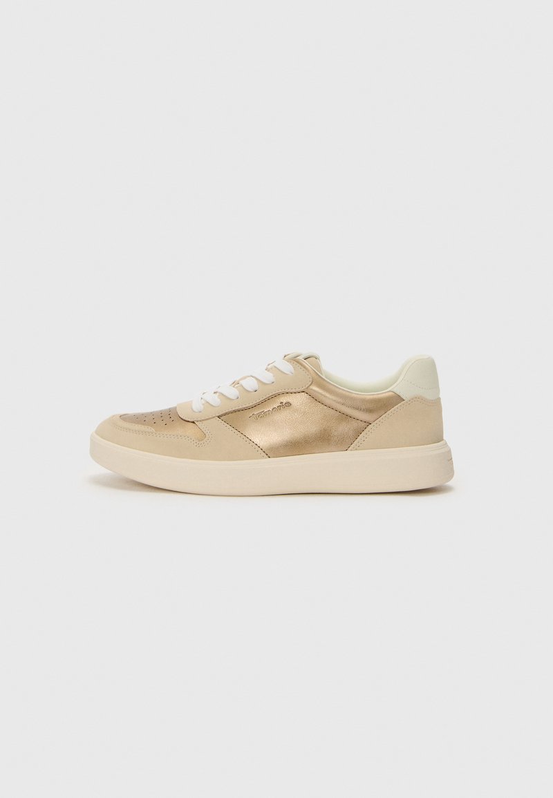 Sneaker with a beige leather upper, metallic accents, white laces, and a textured sole. Features perforated detailing on the toe.