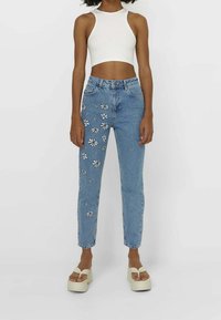 Högmidjade blå jeans med blommig broderi på vänster ben. Tillverkade av denim, med rak benpassform och femficksdesign.