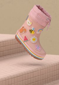 Stivale da pioggia per bambini rosa con adesivi colorati di animali e natura, suola a strisce arcobaleno, fluttuante sopra i gradini piastrellati.