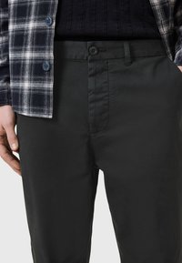 Pantaloni neri in cotone con una texture liscia, dotati di chiusura a pulsante e tasche laterali, abbinati a una camicia a quadri blu navy e bianca.