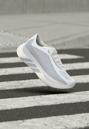 Chaussure de sport blanche et grise capturée en plein air au-dessus d'un passage piéton zébré noir et blanc sur l'asphalte.