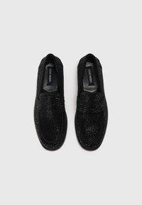 Svarta slip-on skor med en texturerad yta och en glittrande design. Tillverkade av syntetiskt material, med en mjuk innerfoder och rundad form.
