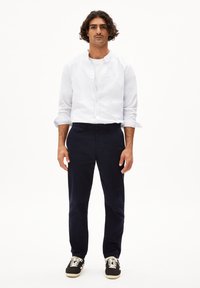 Weißes Hemd mit hochgerollten Ärmeln, kombiniert mit navyfarbenen Hosen und schwarzen Sneakers mit weißen Akzenten. Einfaches, strukturiertes Design.