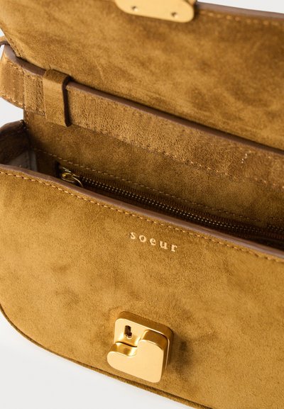 Καφέ τσάντα από σουέντ με χρυσό κούμπωμα, ανοιχτή για να αποκαλύψει εσωτερική τσέπη με φερμουάρ και επένδυση από σουέντ, με την επωνυμία "soeur" σε χρυσά γράμματα.