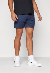 Marineblaue Mesh-Shorts mit elastischem Bund, kombiniert mit weißen High-Top-Sneakers mit schwarzen Logo-Details und weißen Socken.