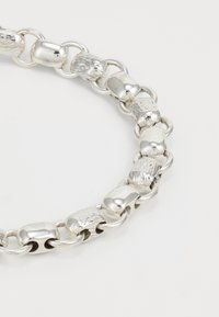 Tuvu skatījums uz sudraba ķēdes aproci ar pārmaiņus gludām un teksturētām taisnstūra saitēm, kas savienotas ar apaļiem gredzeniem.