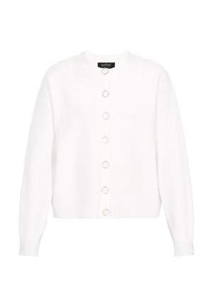 Baltā adītā džemperī ir zeltaini apaļi pogas uz priekšu, ribas aproces un viegla tekstūra ar nedaudz īsu piegriezumu.