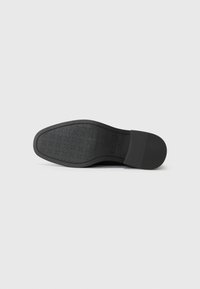 Suela de zapato negra con una superficie texturizada y un patrón geométrico, puntera redonda y un borde liso. El material parece gomoso y duradero.
