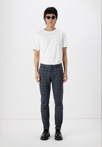 Pantalones de cuadros en blanco y negro con un corte ajustado, combinados con una camiseta blanca lisa y gafas de sol redondas negras. Calzado negro liso.