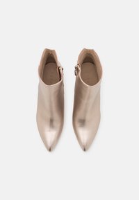Paire de bottines beiges brillantes à bout pointu avec boucles latérales, vues de dessus sur un fond clair.
