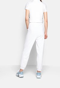 Vit kortärmad T-shirt med en slät yta, kombinerad med vita joggerbyxor med elastiska muddarb. Blå sportskor med texturerade detaljer.