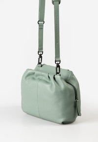 Groene leren crossbody tas met een gestructureerde afwerking, ritssluiting en verstelbare schouderband met zwarte hardwareaccenten en een geplooid bovenontwerp.