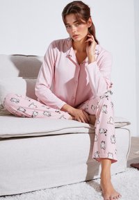 Roze set pidžame s gumbastim gornjim dijelom i hlačama s uzorkom s crtanim mačkama. Mekana tkanina s dugim rukavima i opuštenim krojem.