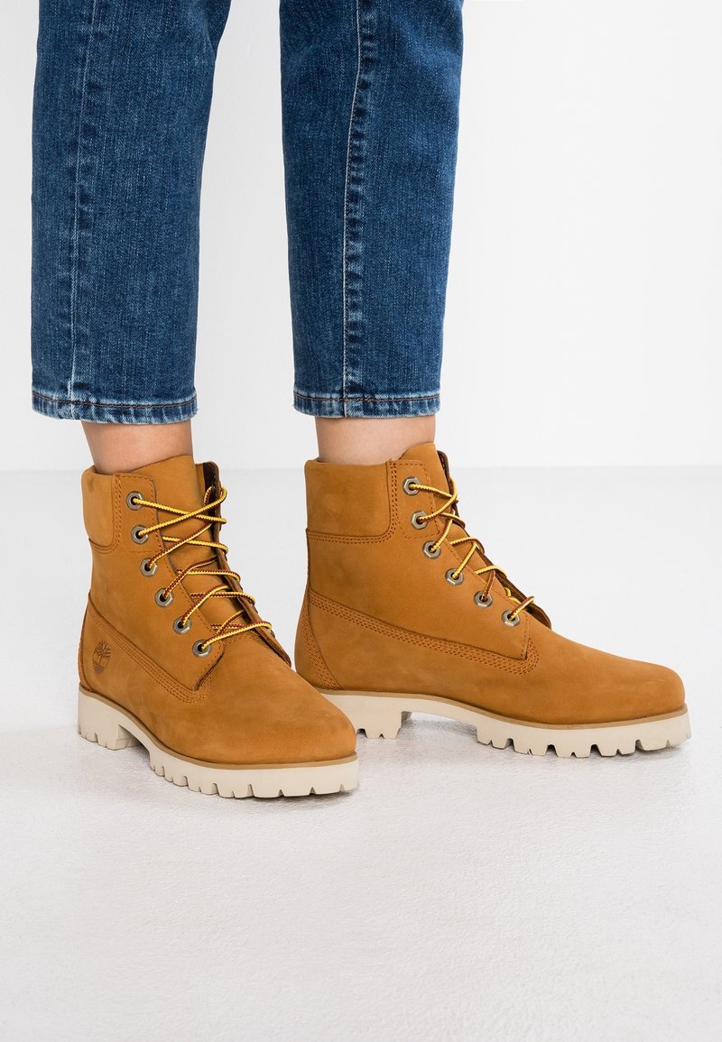 Bottines en suède beige avec des lacets ronds et des semelles en caoutchouc robustes avec un bord blanc contrastant ; comprend un emblème de logo sur le côté.