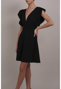 Schwarzes Kleid mit tiefem V-Ausschnitt, flatternden Ärmeln und ausgestelltem Rock. Hergestellt aus glattem Stoff, mit einem taillierten Oberteil und Falten.