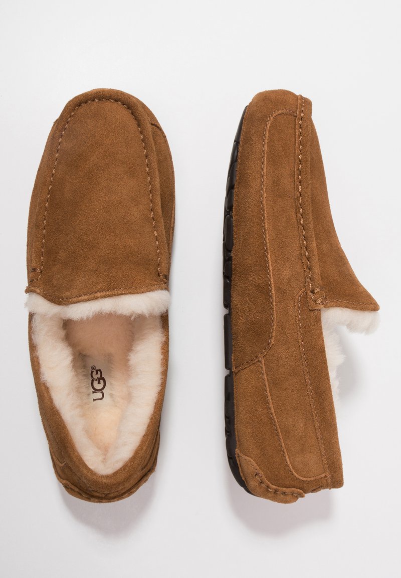 Brown suede slip-on slippers with plush shearling lining, featuring a rounded toe and black rubber sole with textured traction detailing.