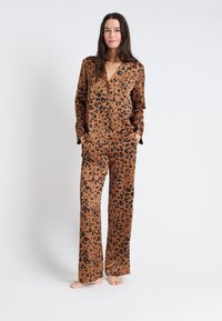 Brązowy zestaw piżamowy w wzór lamparta, wykonany z gładkiego materiału. Posiada długie rękawy, dekolt w serek, dwie przednie kieszenie oraz szerokie spodnie.