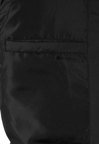 Schwarze gepolsterte Jacke mit einer glatten, glänzenden Textur und einer sichtbaren Tasche. Das Design ist einfach und schnörkellos, wobei die Funktionalität betont wird.