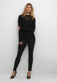 Črn dolg rokav s prosojnim izrezom, v kombinaciji s črnimi teksturiranimi legicami in salonarji s konicami, ki imajo kovinske detajle.