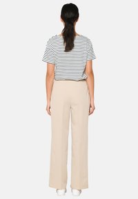 Top a righe a maniche corte bianco e nero abbinato a pantaloni beige a gamba larga. L'outfit presenta una vestibilità rilassata e una trama del tessuto liscia.