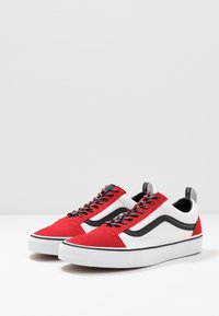 Baskets rouges et blanches avec une tige en daim, des accents noirs et des lacets à motifs. Elles présentent une semelle extérieure en caoutchouc blanc épaisse et une bande latérale signature.