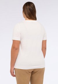 Camiseta blanca de manga corta con cuello redondo, hecha de una tela suave, con una textura lisa y un corte recto en el dobladillo.