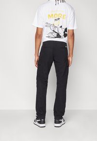 Černé cargo kalhoty s bočními kapsami, spojené s bílým tričkem s grafikou kreslené postavičky jící hůlkami.